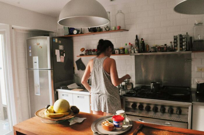 Woman in casual dress preparing food in a kitchen, suggesting a scene of dealing with difficult roommates at home.