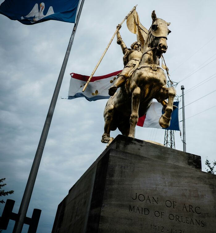 Statue of Joan of Arc on horseback with flags in the background depicting crazy but real historical events.