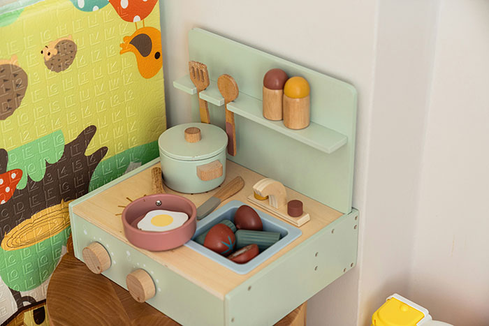 Wooden toy kitchen with stove, pot, frying pan, and vegetables illustrating classic school moments.