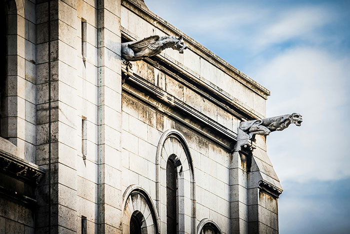 Stone gargoyle statues on an old building facade representing creepy and disturbing stories from morticians.