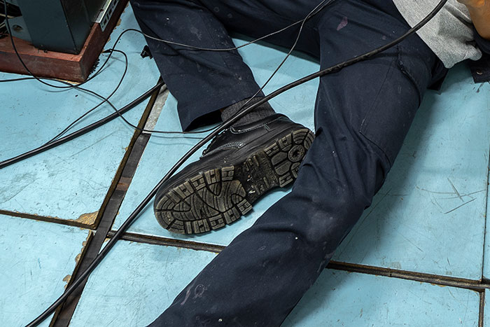 Person lying on blue tiled floor with dark pants and black shoes tangled in black cables, creepy and disturbing mortician scene
