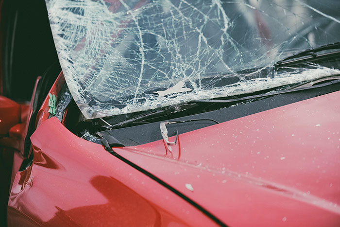 Red damaged car with shattered windshield symbolizing creepy and disturbing stories from morticians and accident scenes.