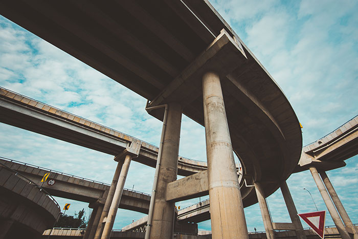 Curved concrete overpass and highway ramps under a partly cloudy sky with towering support columns.