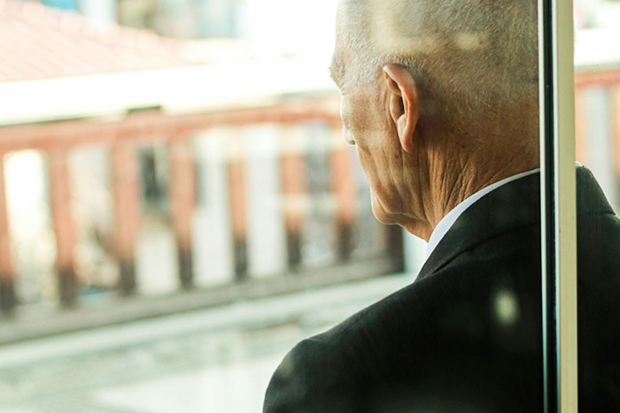 Elderly man in a suit looking out window, evoking a somber mood related to creepy and disturbing stories from morticians.