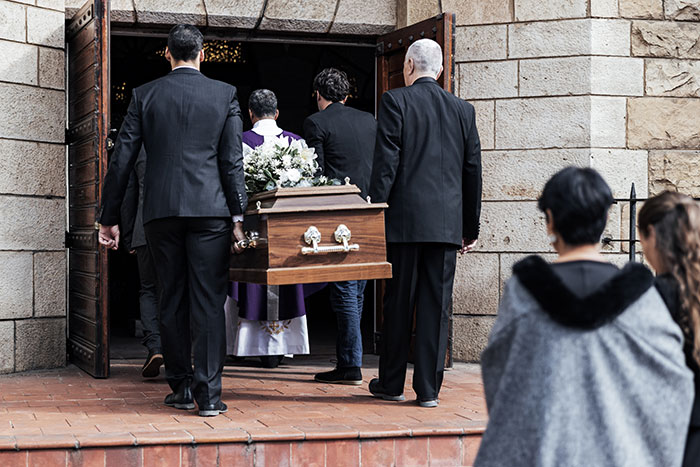 Pallbearers carrying a coffin into a stone building during a funeral, illustrating creepy and disturbing mortician stories.
