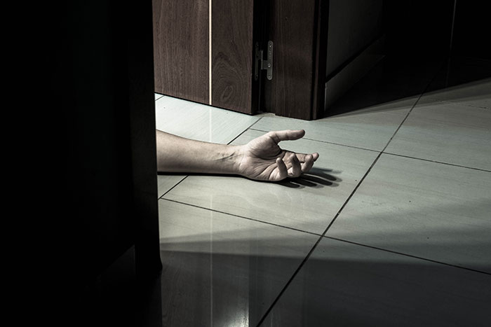 A lifeless hand on a tiled floor near a partially open door, evoking creepy and disturbing mortician stories.