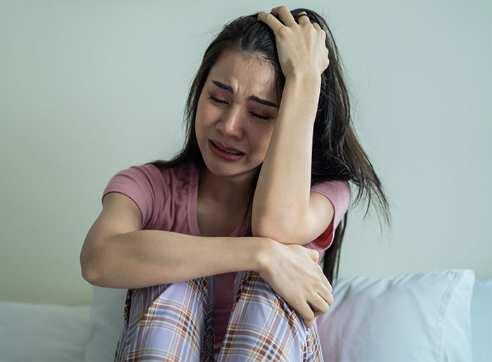 Young woman upset and crying at home, distressed over family vacation spending and causing jealousy among cousins.