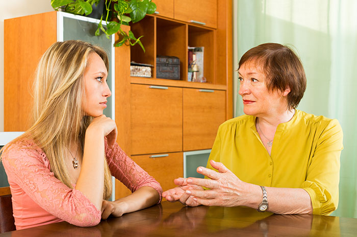 Woman accusing her mother of embezzling inheritance, confronting her at home with serious expressions and tense body language.