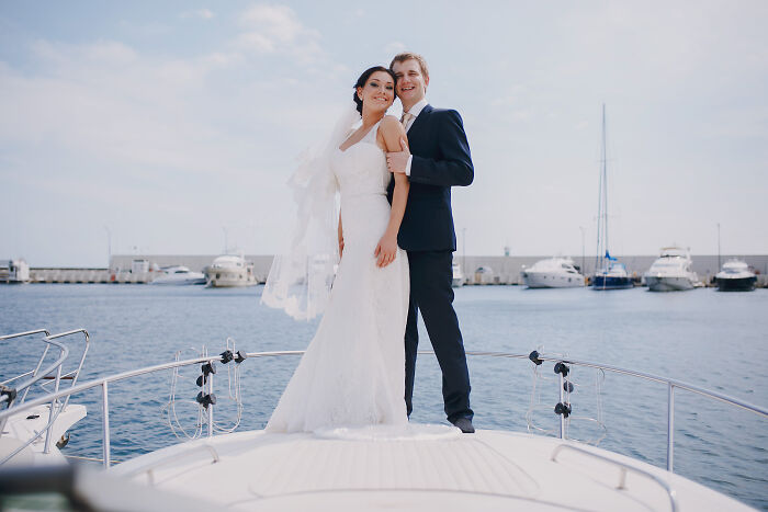 Bride and groom standing on a boat, celebrating a wedding with water and yachts in the background. - 31