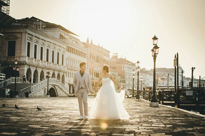 A bride and groom holding hands outdoors at sunset, capturing moments of going to the same person’s multiple weddings. - 21
