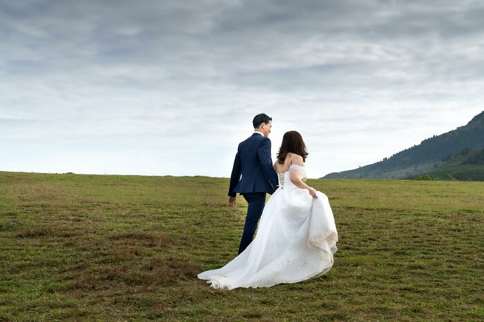 Bride in white wedding dress and groom in blue suit walking on a grassy field, symbolizing stories of second and third weddings. - 27