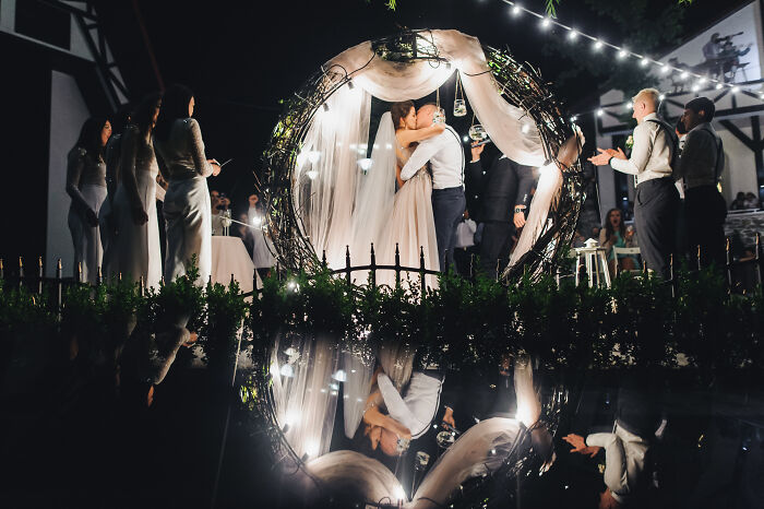 Couple kissing under a decorated arch at a wedding ceremony with guests applauding, reflecting the theme of second weddings. - 26