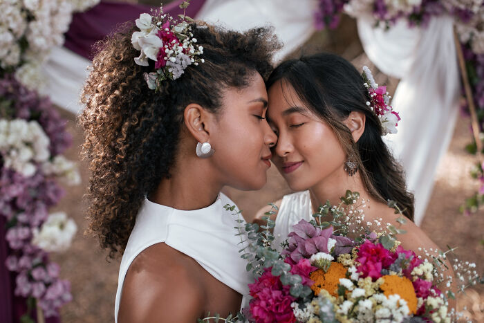 Two brides with floral hairpieces sharing a tender moment, surrounded by wedding flowers at a wedding celebration. - 16