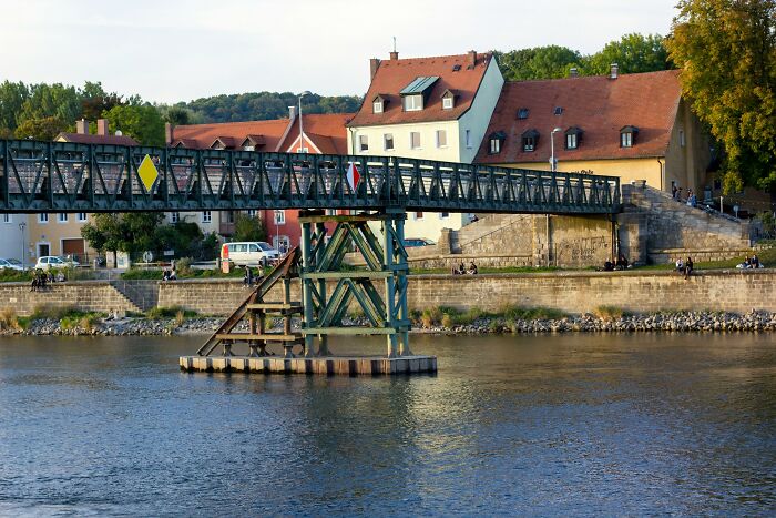 A rusting bridge over a river with old houses in the background, representing structures on the brink of collapse. - 10