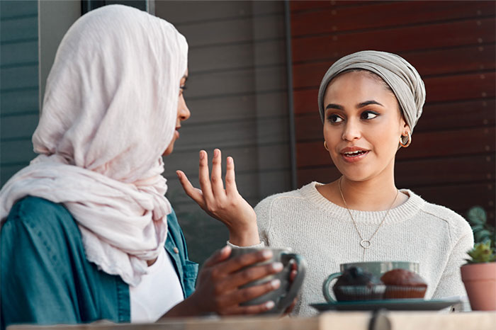 Two women wearing headscarves having coffee and discussing borderline racism in a casual cafe setting. Two women wearing headscarves having coffee and discussing borderline racism in a casual cafe setting.