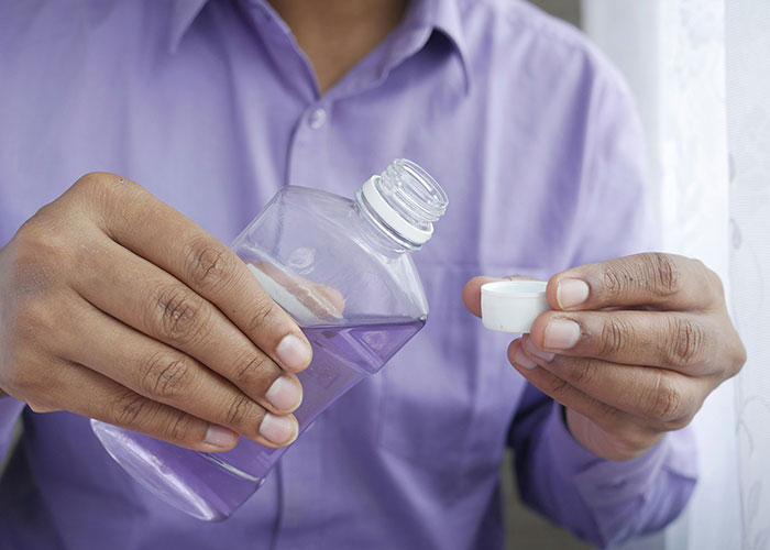 Person in purple shirt pouring liquid from a clear bottle into a small white cap, illustrating marketing campaign concept.