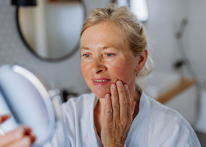 Middle-aged woman looking at her reflection in a handheld mirror, illustrating themes of marketing campaigns and perception.