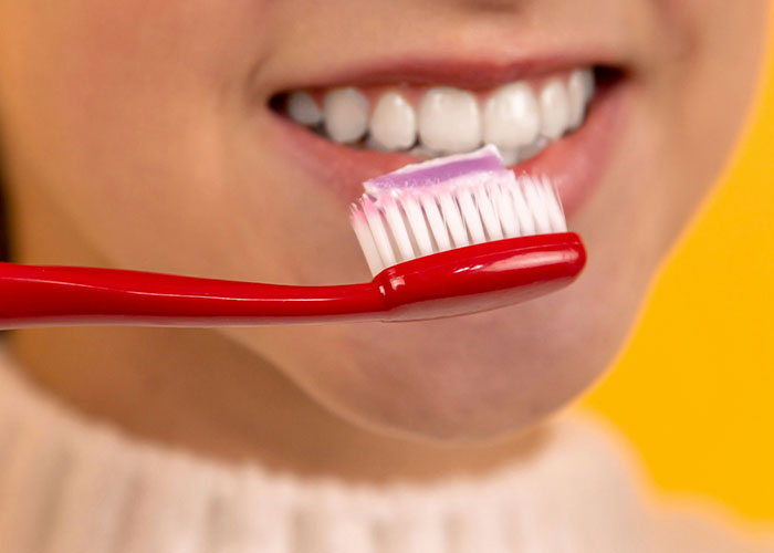 Close-up of a person smiling with white teeth, holding a red toothbrush with purple toothpaste, illustrating marketing campaigns.