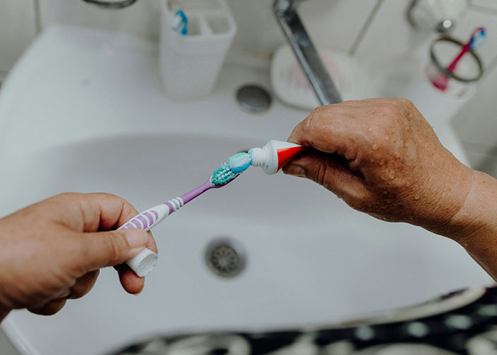 Person applying toothpaste onto a toothbrush emphasizing powerful marketing campaigns in everyday routines.