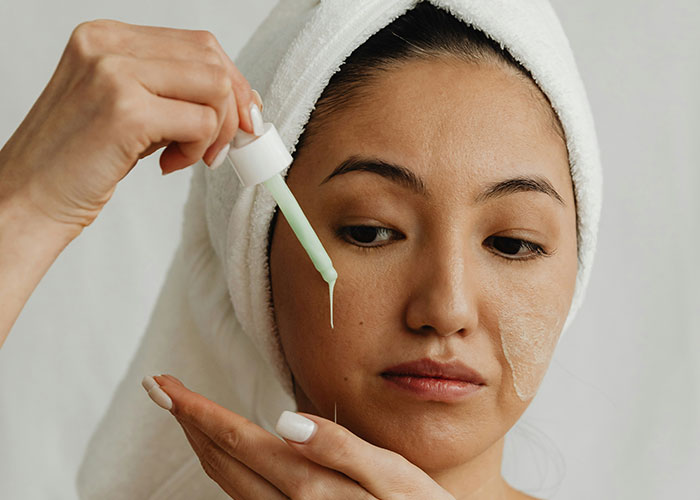 Woman with towel on head applying green skincare serum, illustrating marketing campaigns with powerful visual storytelling.