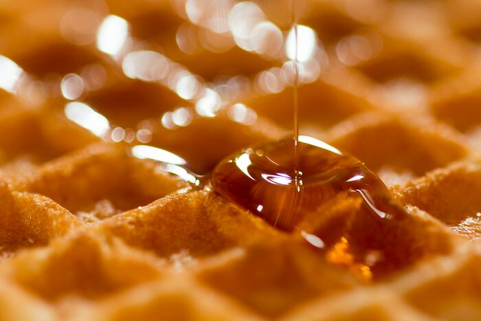 Close-up of syrup being poured on a golden waffle, illustrating a bizarre fact about countries shared by people.