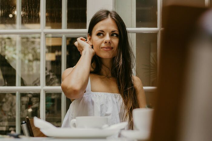 Woman sitting at a table by a window, thoughtfully looking sideways, related to what makes a man instantly unattractive to women.