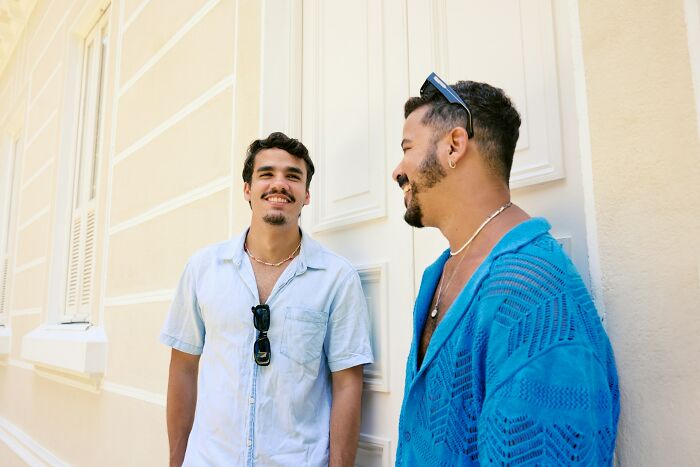 Two young men casually talking outside near a light yellow wall, representing people who ran away from home stories. - 26