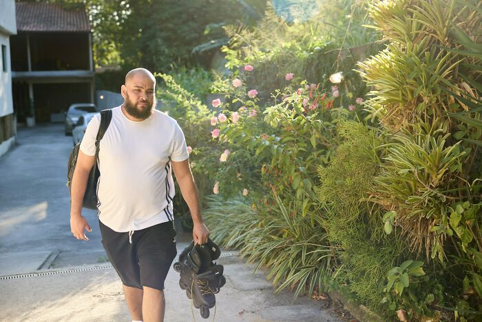 Man walking outdoors holding rollerblades and backpack, illustrating things men find normal but seem bizarre to women.