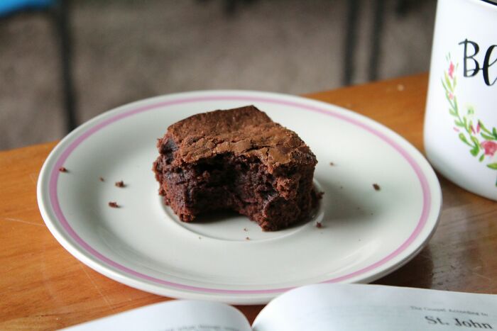Partially eaten brownie on a plate next to a coffee mug and an open book, illustrating revenge on bosses concept. - 16