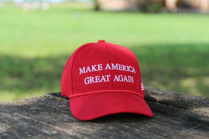Red Make America Great Again hat resting on a weathered wooden surface in an outdoor setting.