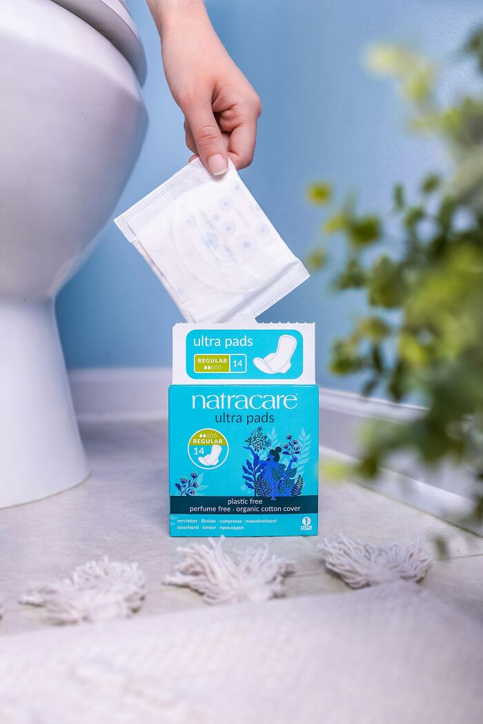 Hand holding a sanitary pad above a trash bin in a bathroom, illustrating awful roommate hygiene issues.