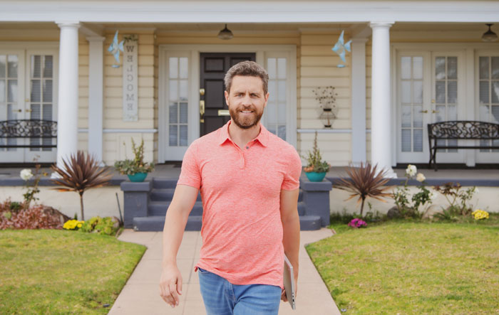 Man helping domestic violence victim walks confidently in front of a suburban home with garden plants and a porch.