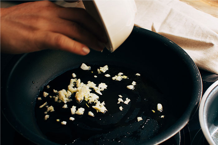 Hand pouring chopped garlic into a frying pan with oil, illustrating cooking secrets and ingredients shared by home cooks. - 15