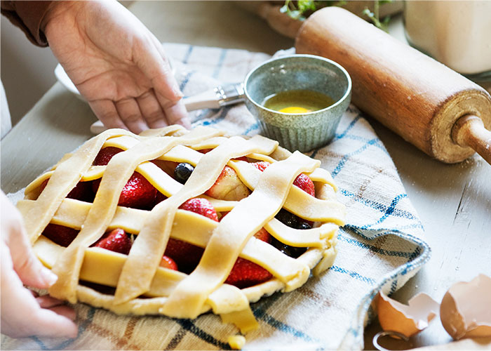 Hands placing a lattice-topped fruit pie on a cloth, highlighting cooking secrets and ingredients in homemade baking. - 13
