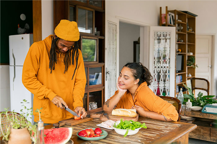 Two people in a cozy kitchen sharing cooking secrets while preparing fresh ingredients on a wooden table. - 3