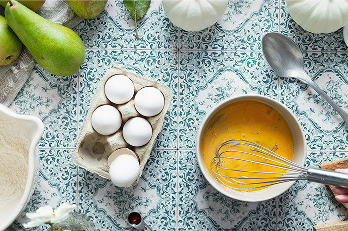 Whisking eggs in a bowl with fresh ingredients on patterned surface, sharing cooking secrets and hidden ingredients. - 41