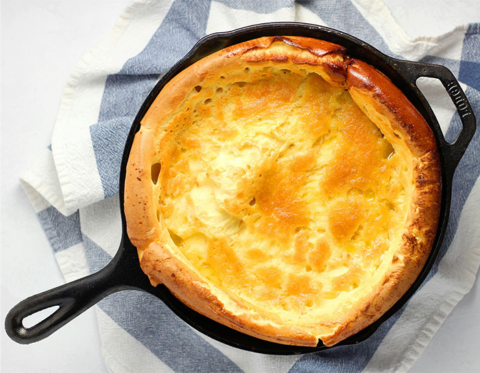 Dutch baby pancake cooked in a cast iron skillet, showcasing a golden crust with cooking secrets and ingredients revealed. - 44