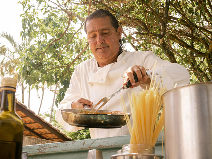 Chef cooking outdoors, sharing cooking secrets and unique ingredients while preparing a dish with spaghetti nearby. - 46