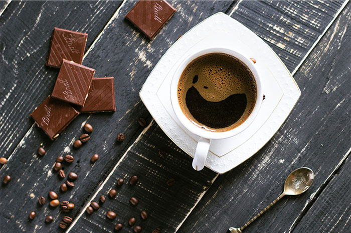 Cup of coffee on a saucer with pieces of chocolate and scattered coffee beans, illustrating cooking secrets and ingredients. - 24