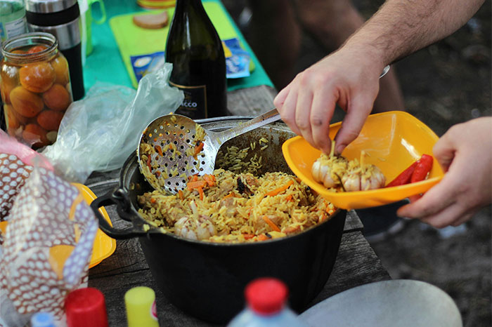 Person serving seasoned rice with secret cooking ingredients from a large pot in an outdoor cooking setting - 28