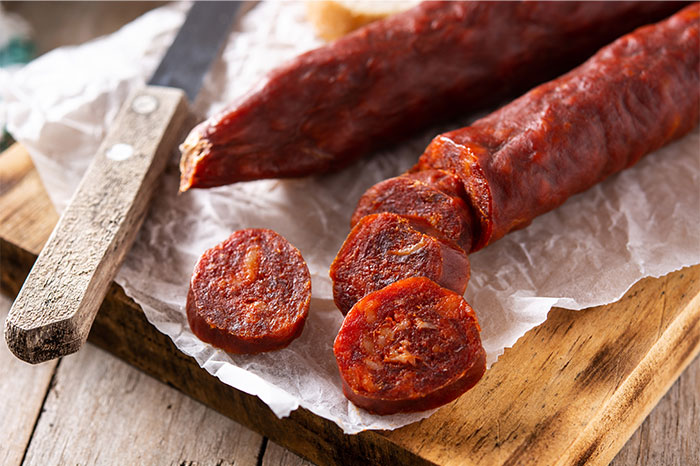 Close-up of sliced spicy sausage on parchment paper with a knife, highlighting cooking secrets and ingredients. - 31