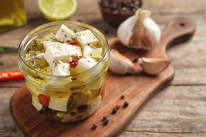 Glass jar filled with marinated cheese and herbs on a wooden board, showcasing cooking secrets and unique ingredients. - 19