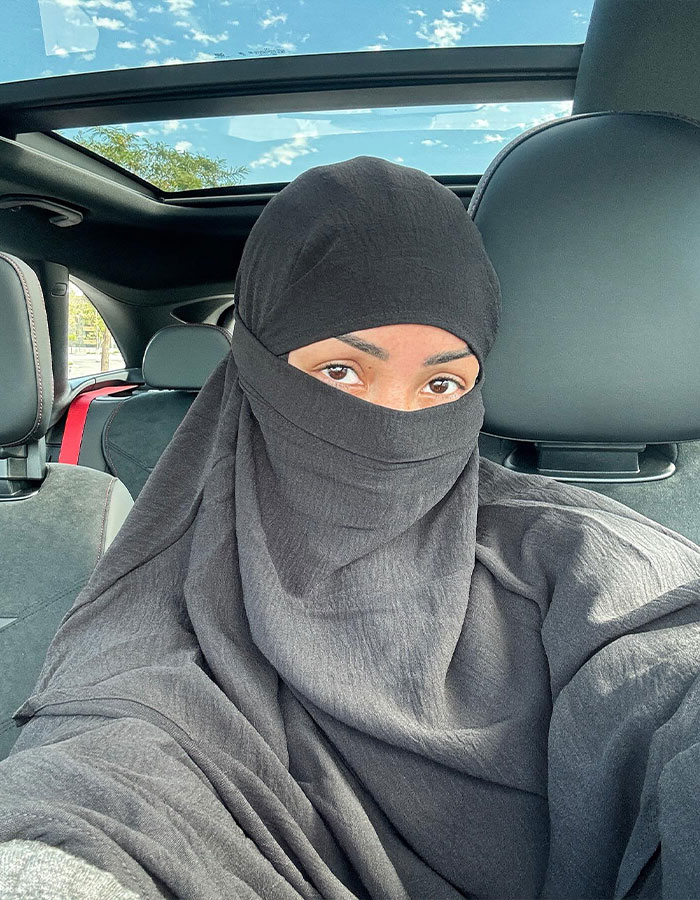 Woman wearing a black hijab inside a car with a sunroof, reflecting on the influence of hijab in fashion and identity. Woman wearing a black hijab inside a car with a sunroof, reflecting on the influence of hijab in fashion and identity.