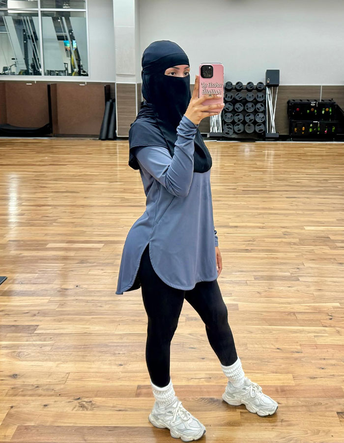 Woman wearing hijab and modest activewear taking a selfie in an empty gym with wooden flooring and fitness equipment. Woman wearing hijab and modest activewear taking a selfie in an empty gym with wooden flooring and fitness equipment.