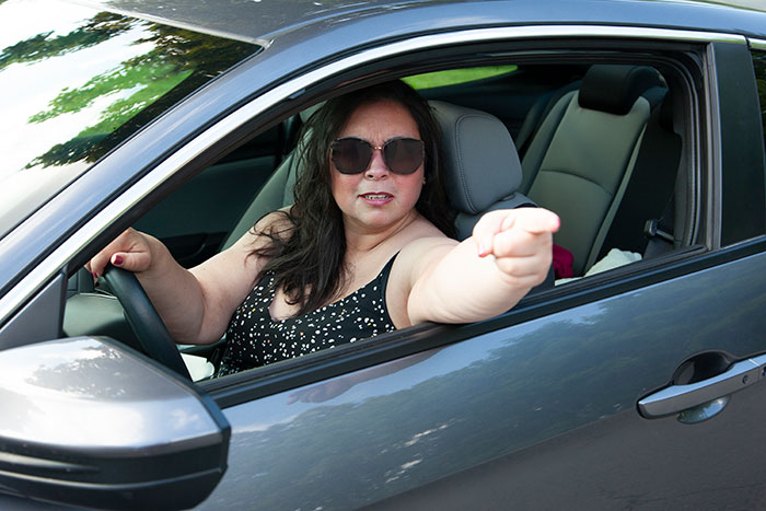Woman in sunglasses driving car, pointing outside, representing disabled woman and neighbor driveway dispute.