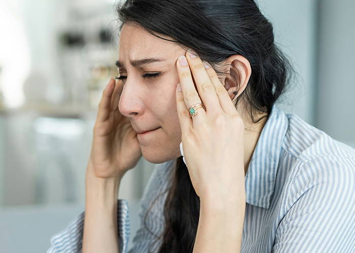 Young woman in striped shirt holding her head, upset about her friend getting fired and consequences that followed.