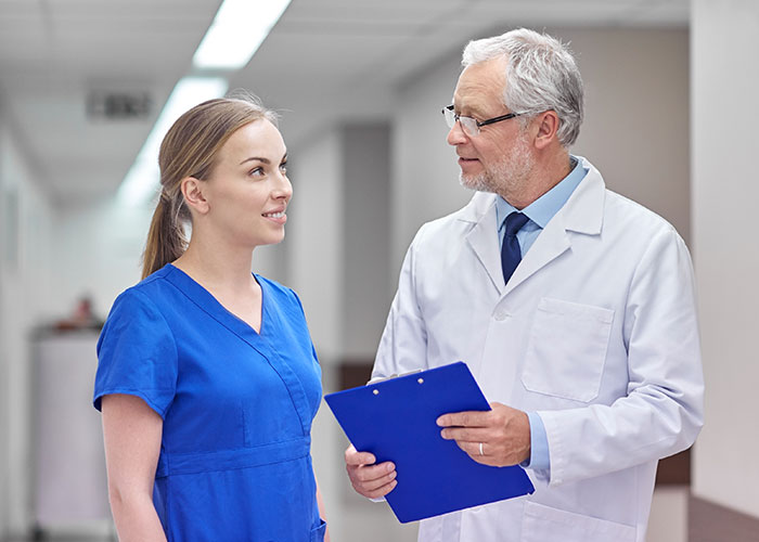 Male doctor holding clipboard talking to female nurse in hospital hallway discussing nurse workplace issues. Male doctor holding clipboard talking to female nurse in hospital hallway discussing nurse workplace issues.