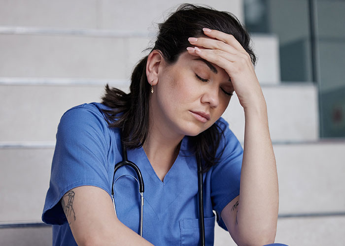 Stressed nurse sitting on stairs with hand on forehead, reflecting on controversy involving new nurse and family accusation. Stressed nurse sitting on stairs with hand on forehead, reflecting on controversy involving new nurse and family accusation.