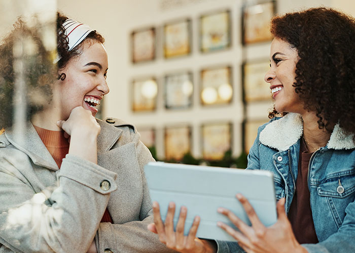 Two women, one dressed as a nurse, smiling and discussing content on a tablet in a casual setting. Two women, one dressed as a nurse, smiling and discussing content on a tablet in a casual setting.