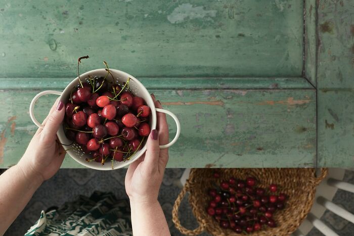 Hands holding a bowl of cherries over a rustic table, illustrating mysterious body quirks people can’t find answers for.